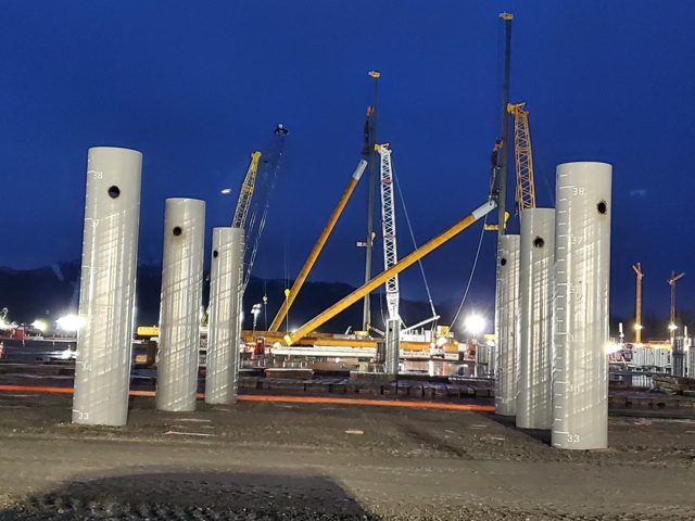 Large-diameter pipe piles standing ready for night installation at an LNG facility